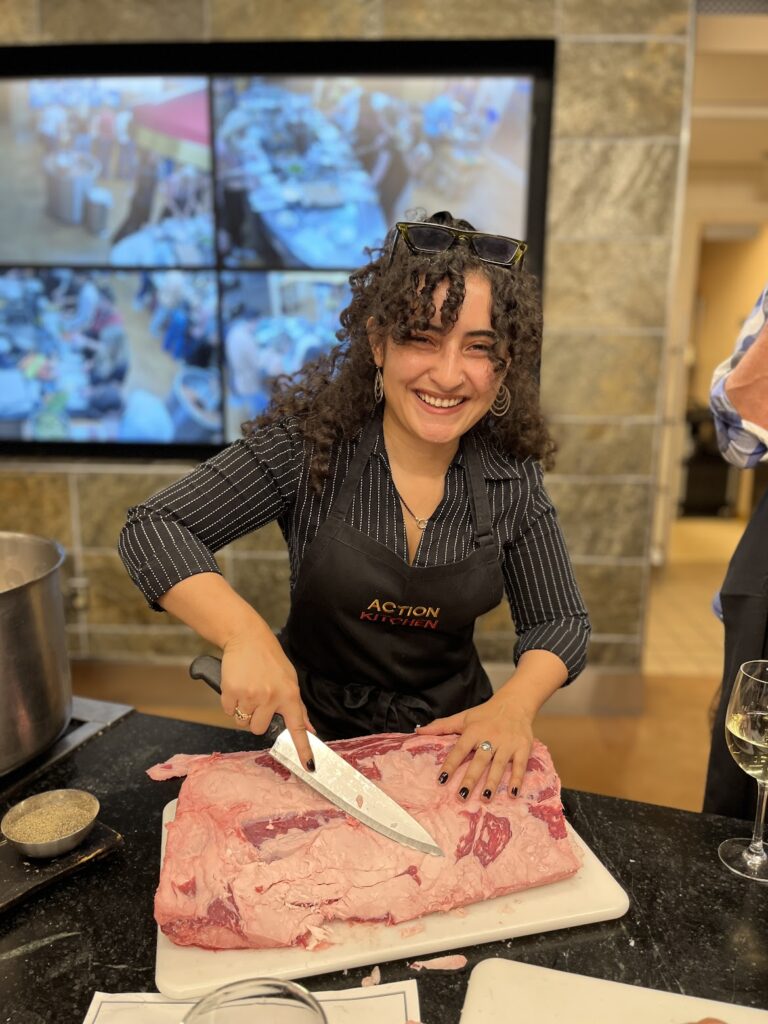 A woman with an apron and a large knife cutting up a piece of meat